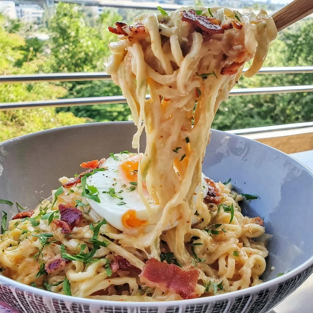 Bowl of Viral Carbonara Spicy Chicken Ramen garnished with herbs and spices.
