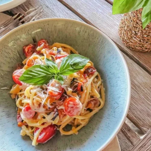A bowl of delicious tomato basil pasta topped with fresh basil and tomatoes.