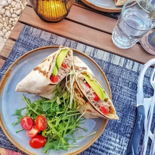 Tuna flatbread topped with avocado and tomato on a rustic wooden table.
