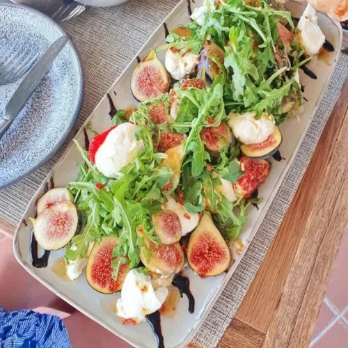 Irresistible burrata appetizer with figs and arugula on a stylish platter.
